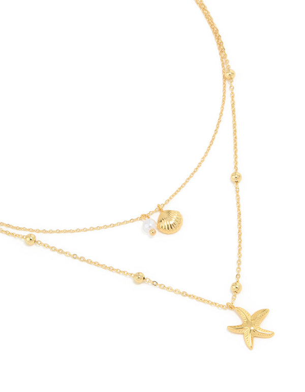 Showcasing a waterproof gold plated stainless steel layered necklace with balls, ocean-inspired shell and star charms in gold close up view