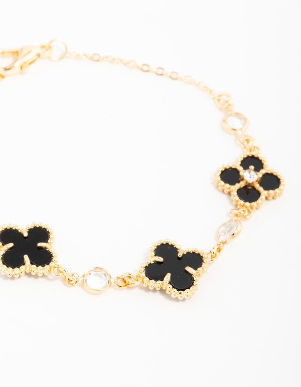 Highlighting a gold plated cubic zirconia black flower charm bracelet with dainty details close up view
