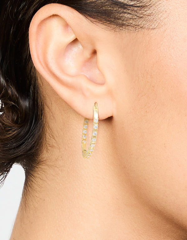 Crafted from gold plated material, these statement large skinny hoop earrings with cubic zirconia are shown on ear view