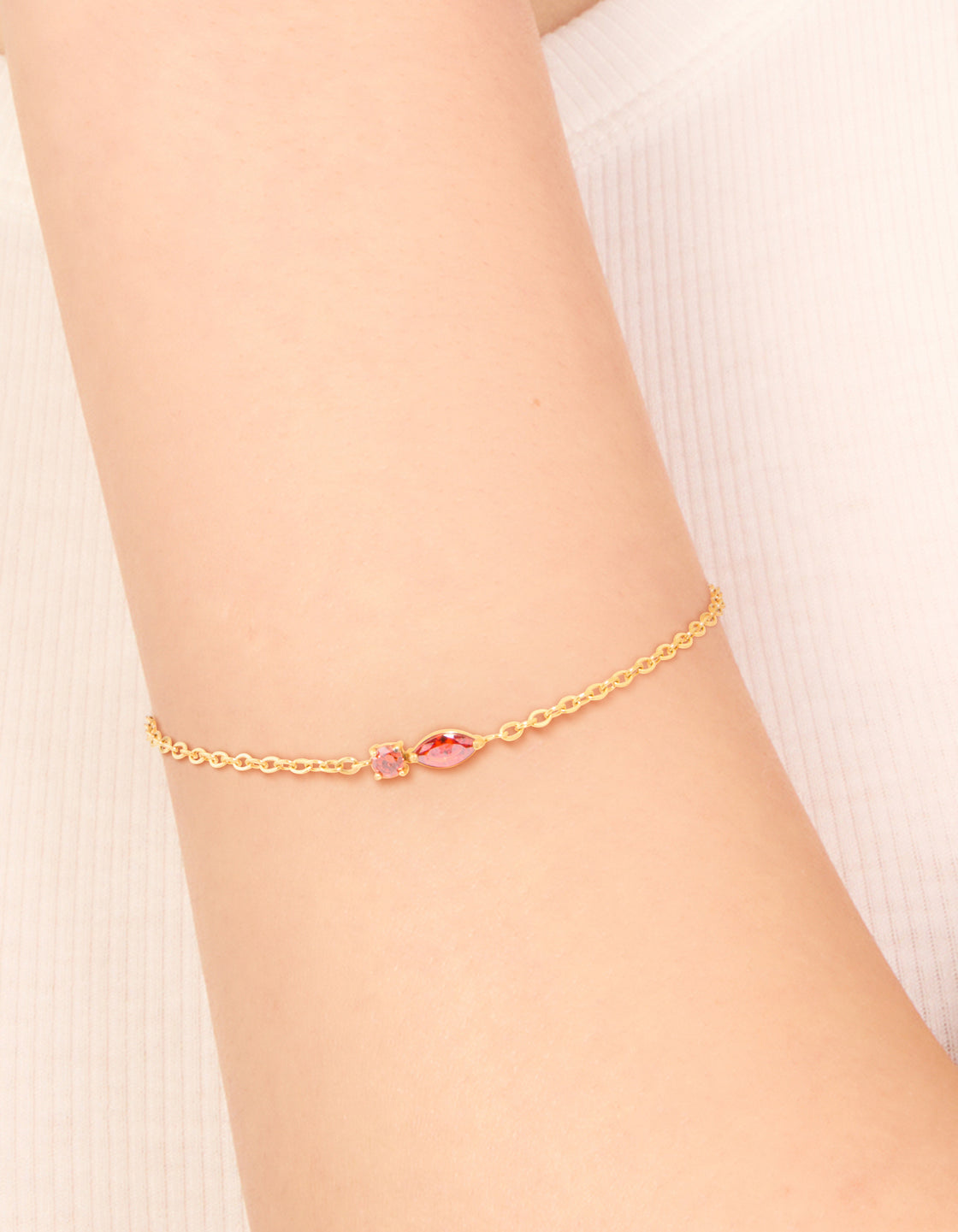 Showcasing waterproof gold plated stainless steel July red cubic zirconia birthstone bracelet in dainty style on wrist view