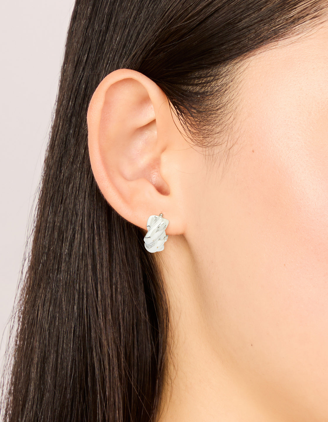 Featuring waterproof stainless steel twisted hoop earrings in silver on ear view