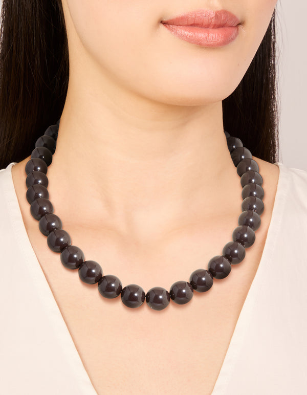 Featuring a chocolate brown acrylic beaded necklace in gold accents on neck view