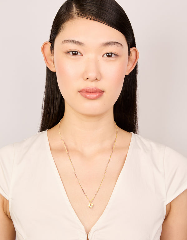 Featuring a waterproof bubble letter U initial pendant necklace in gold plated stainless steel with a dainty style on model view