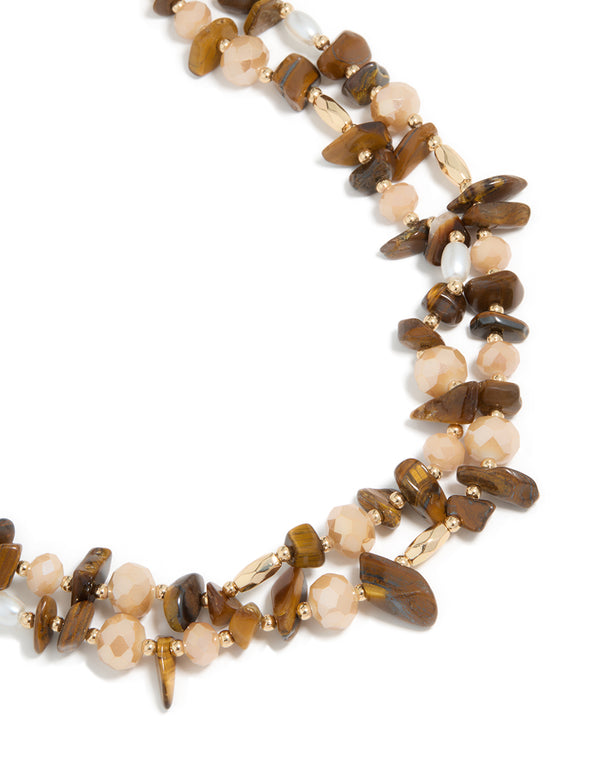 Showcasing an acrylic beaded and tigers eye semi precious stone boho layered necklace featuring brown, peachpuff, and gold tones close up view