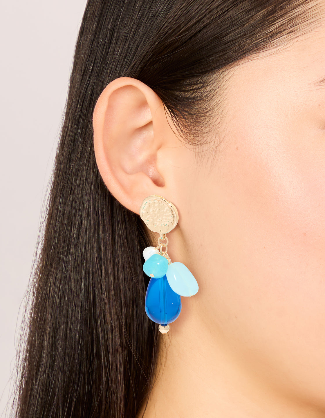 Showcasing gold textured and blue beaded drop earrings with charms featuring statement style on ear view