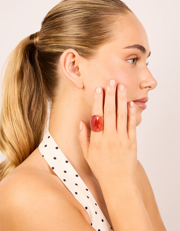 Showcasing statement acrylic rings in coral and orange with floral gold accents, 3-pack on finger view