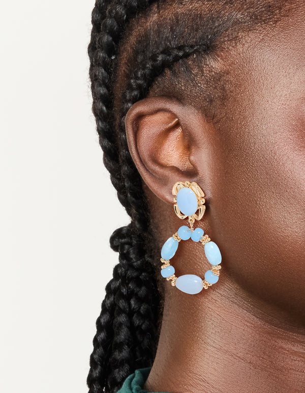 Showcasing gold light blue beaded oval drop earrings with on ear view