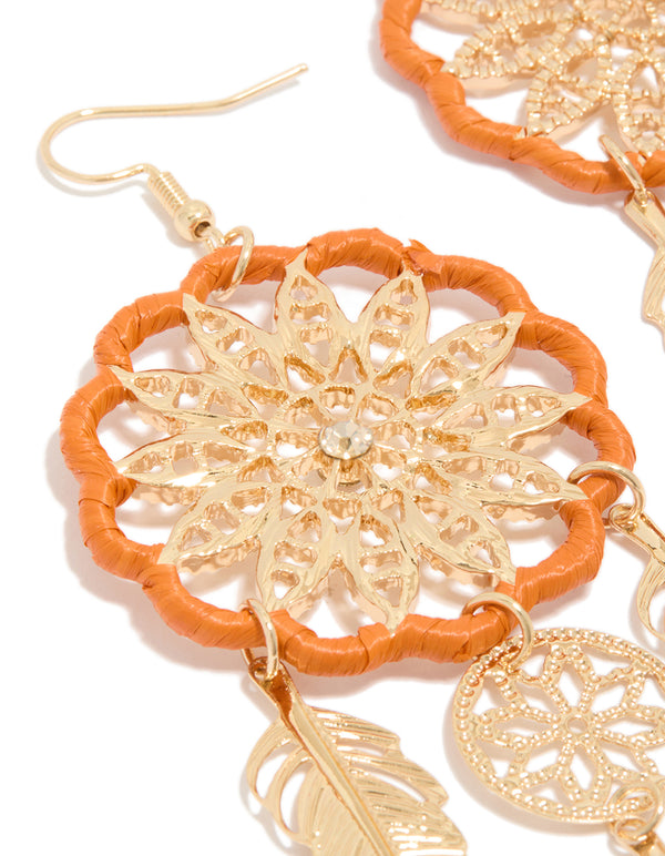 Showcasing gold orange yarn dreamcatcher feather drop earrings with statement charm close up view