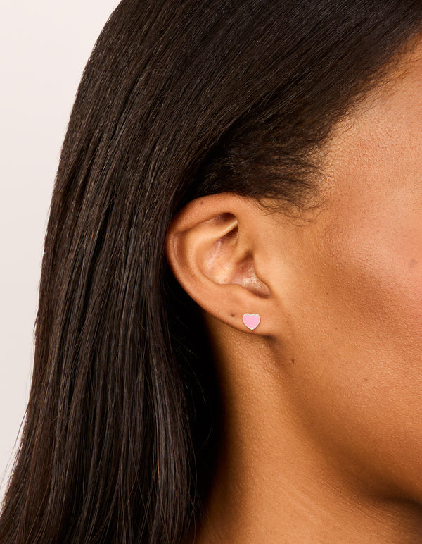 Showcasing dainty sterling silver pink enamel heart stud earrings featuring stud closure in silver on ear view
