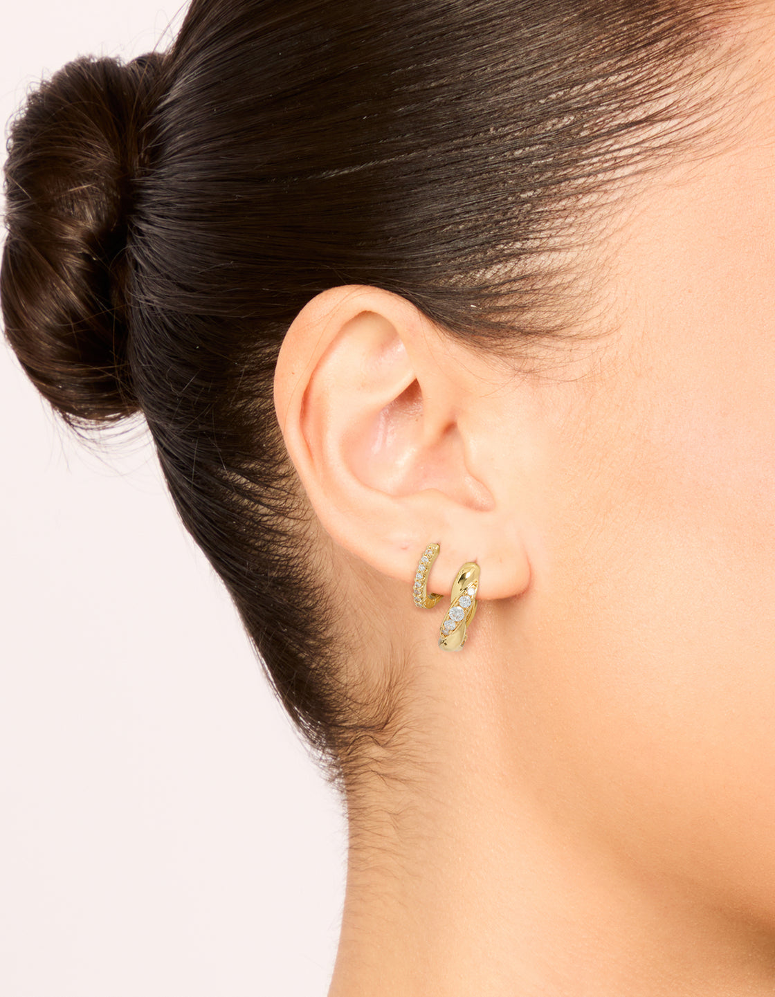 Crafted from gold plated brass, these woven and fine cubic zirconia huggie earrings with crystal accents are shown in a 2-pack on ear view