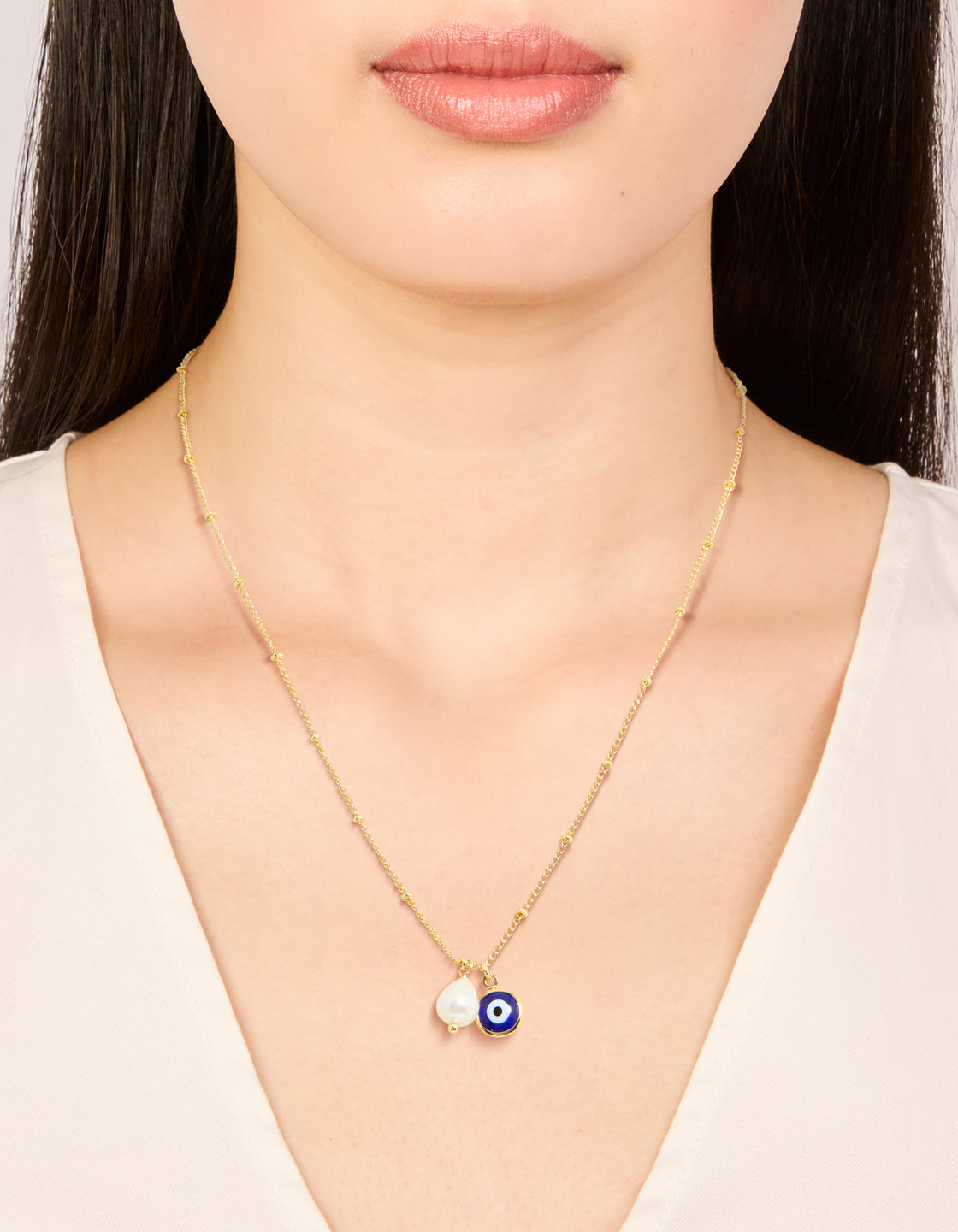 Crafted from gold plated brass, this pearl and evil eye pendant necklace features beaded chain with charm accents on neck view