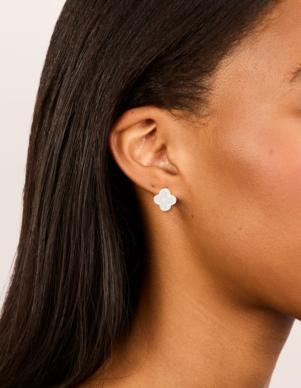 Showcasing dainty small floral stud earrings crafted from silver plated metal with cubic zirconia in white on ear view