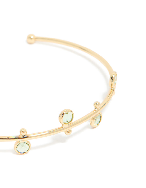 Featuring a gold plated and green cubic zirconia wrist cuff in a statement style, close up view