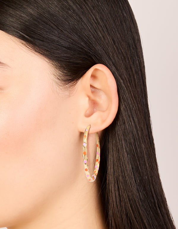 Showcasing large statement hoop earrings with enamel dotted design in pink and orange on thin closure on ear view