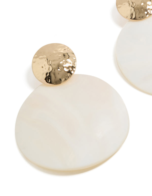 Close up of hammered gold texture and white genuine shell disc in statement ocean-inspired drop earrings close up view