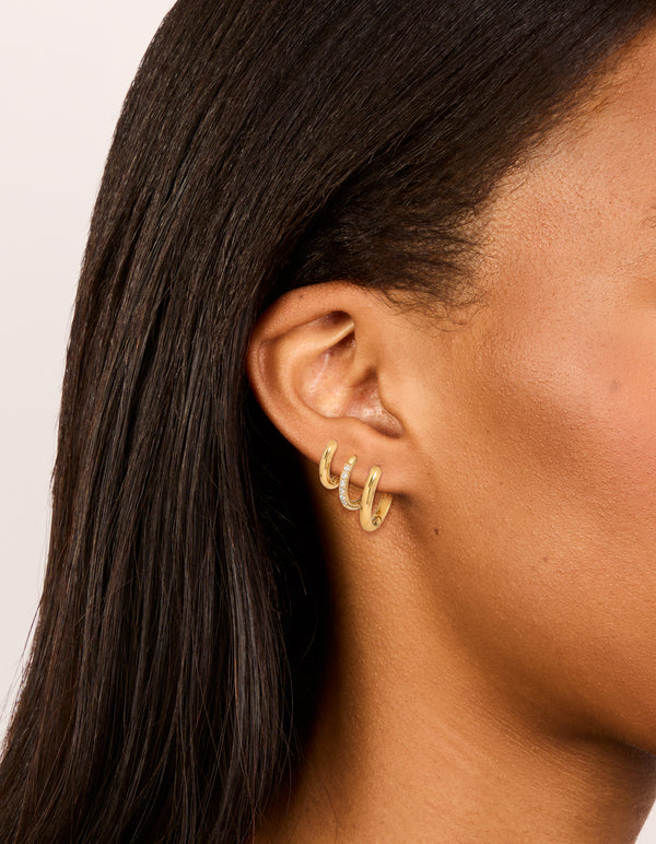 Showcasing waterproof gold plated stainless steel cubic zirconia essential stacking huggie earrings in a 3-pack with crystal accents and closure on ear view