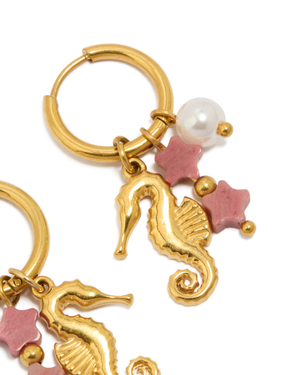 Showcasing waterproof gold plated stainless steel seahorse pearl charm huggie earrings with ocean celestial elements featuring in light pink and white close up view
