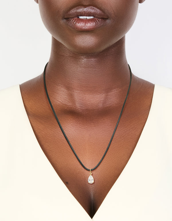 Showcasing a waterproof necklace with gold plated stainless steel and black cord and pear cut cubic zirconia pendant in crystal on neck view