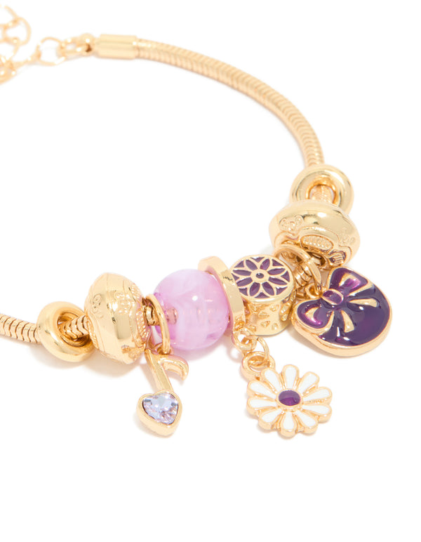 This gold bow and music note charm bracelet showcases beads, floral elements, and heart details in purple, pink, and white close up view