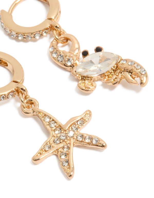 Detailed view of mismatched gold huggie earrings with ocean details and crystal embellishments close up view