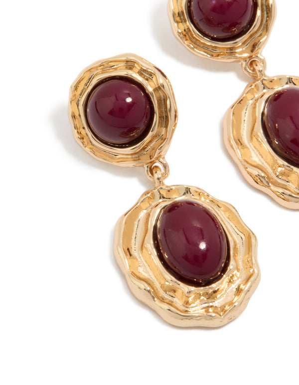 Showcasing statement gold double burgundy resin drop earrings with textured metal framing and maroon stones close up view