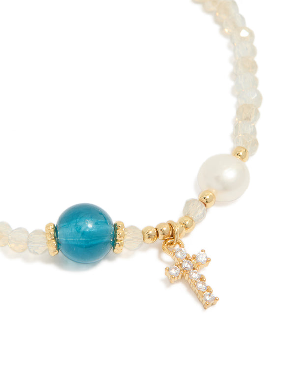 Designed with gold plated metal, this dainty beaded bracelet features a cross charm with cubic zirconia, freshwater pearl accents, and turquoise beige white details close up view