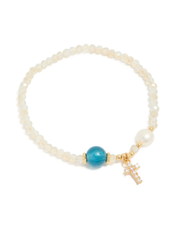 Crafted from gold plated metal, this dainty beaded bracelet features a cross charm with cubic zirconia, freshwater pearl accents, and turquoise beige white details front view