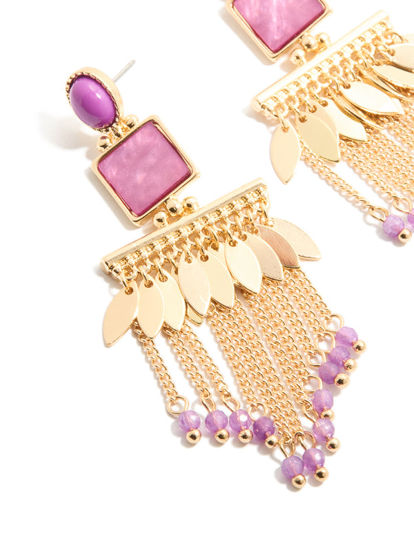 Highlighting statement drop earrings in gold with purple oval stones, leaf charms and beaded chain tassels in close up view
