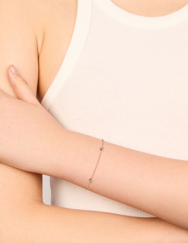Showcasing a gold plated bracelet featuring blue teardrop cubic zirconia with dainty chain and adjustable closure on wrist view