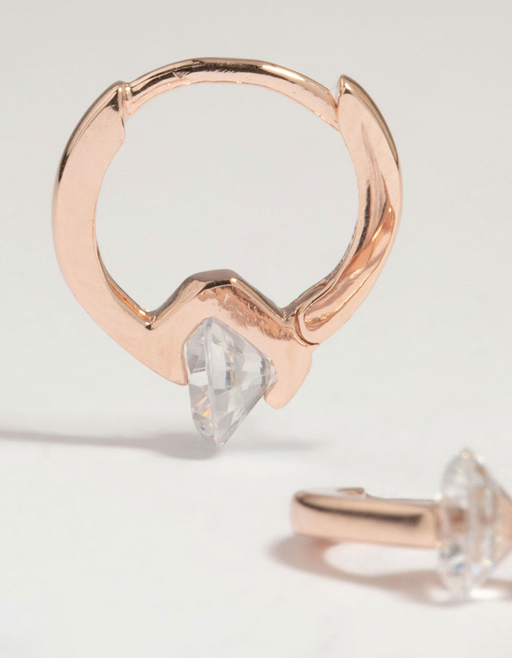 Highlighting rose gold plated sterling silver cubic zirconia huggie earrings with round stone cut close up view