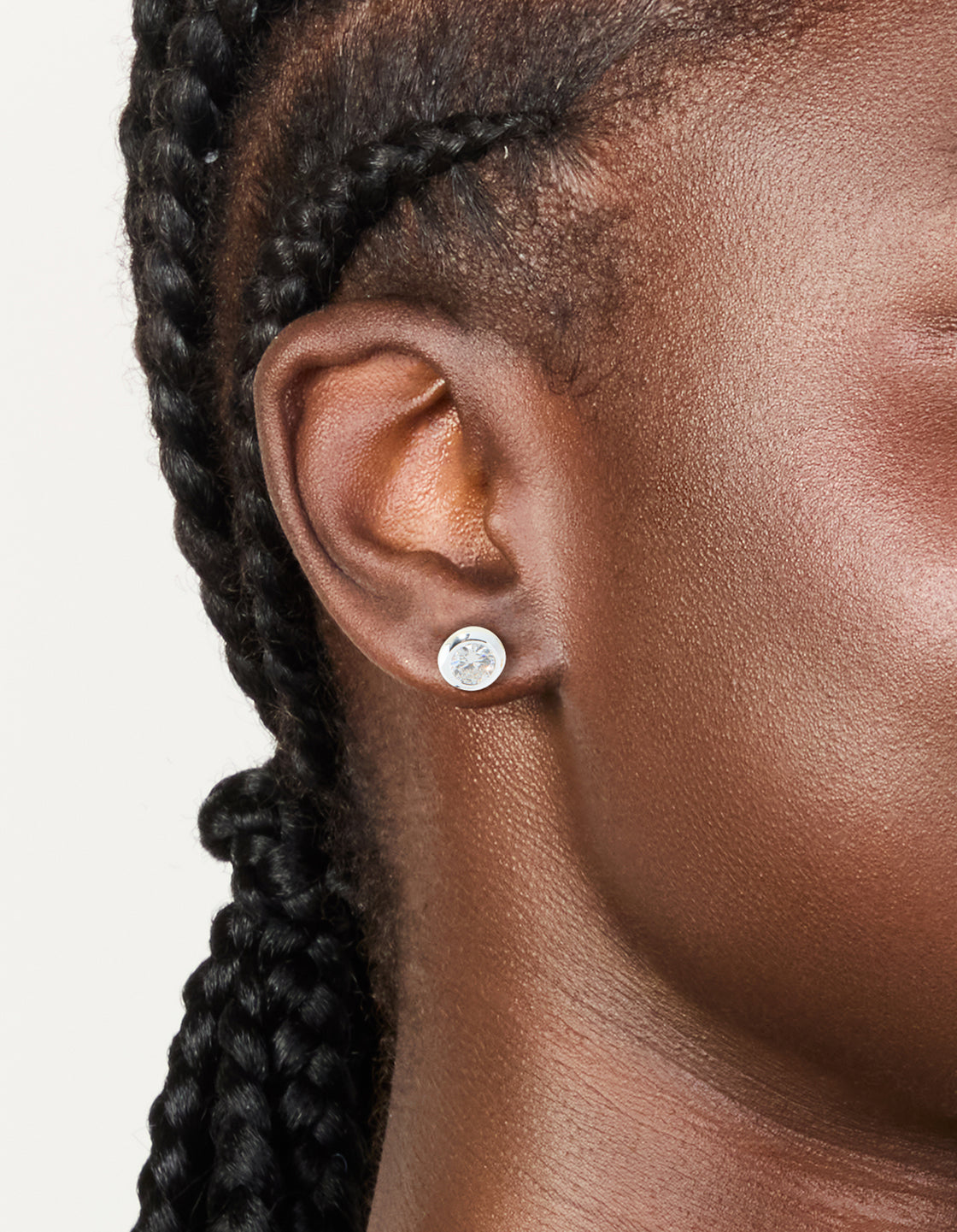 Featuring waterproof stainless steel round cubic zirconia bezel-set earrings with crystal in silver and clear on ear view