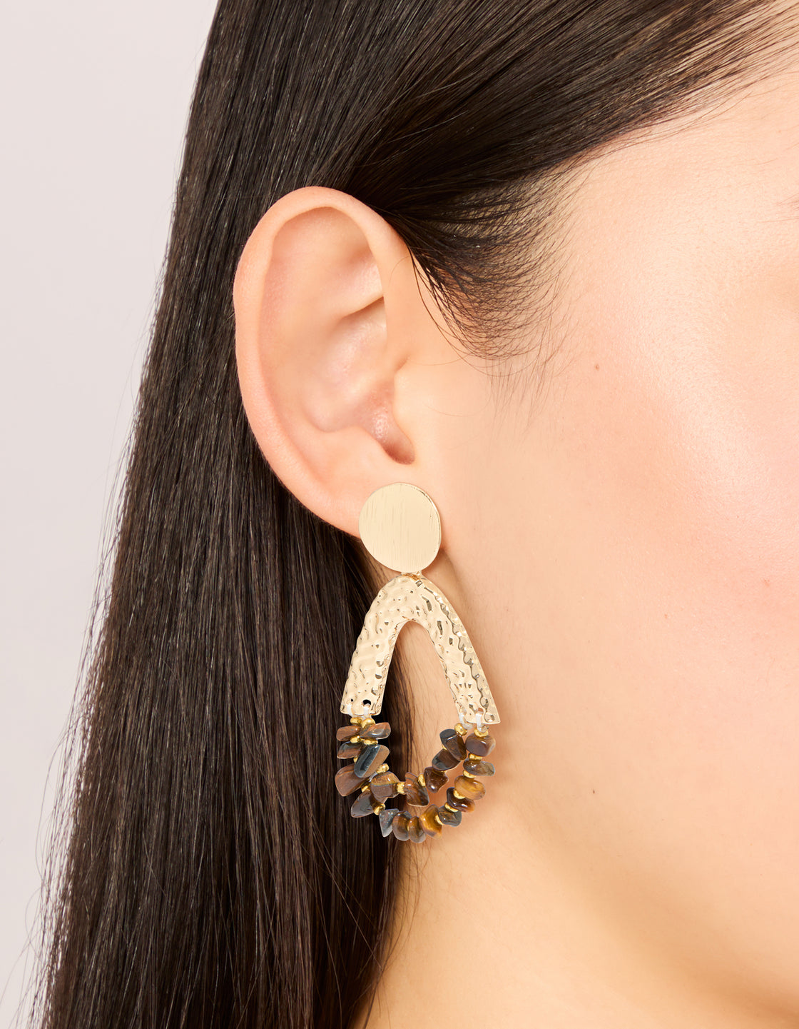 Showcasing statement earrings with tigers eye semi precious stone chip beads and molten drop design in gold on ear view