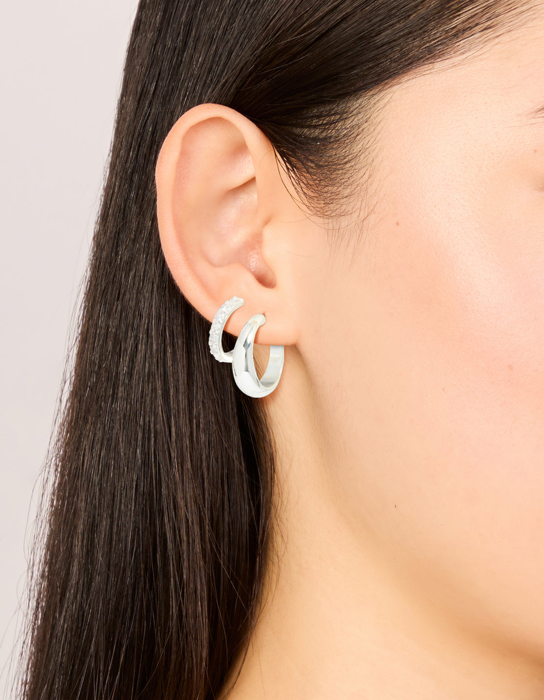 Showcasing silver plated cubic zirconia and smooth hoop earrings in a 2-pack with crystal accents on ear view