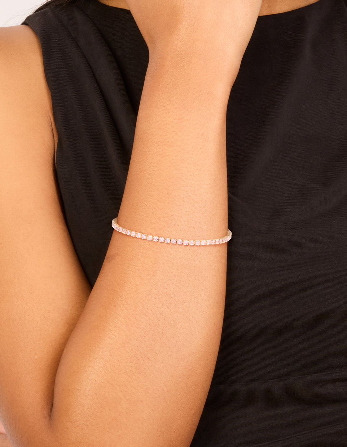 Showcasing a gold pink cubic zirconia dainty tennis bracelet in light pink on wrist view