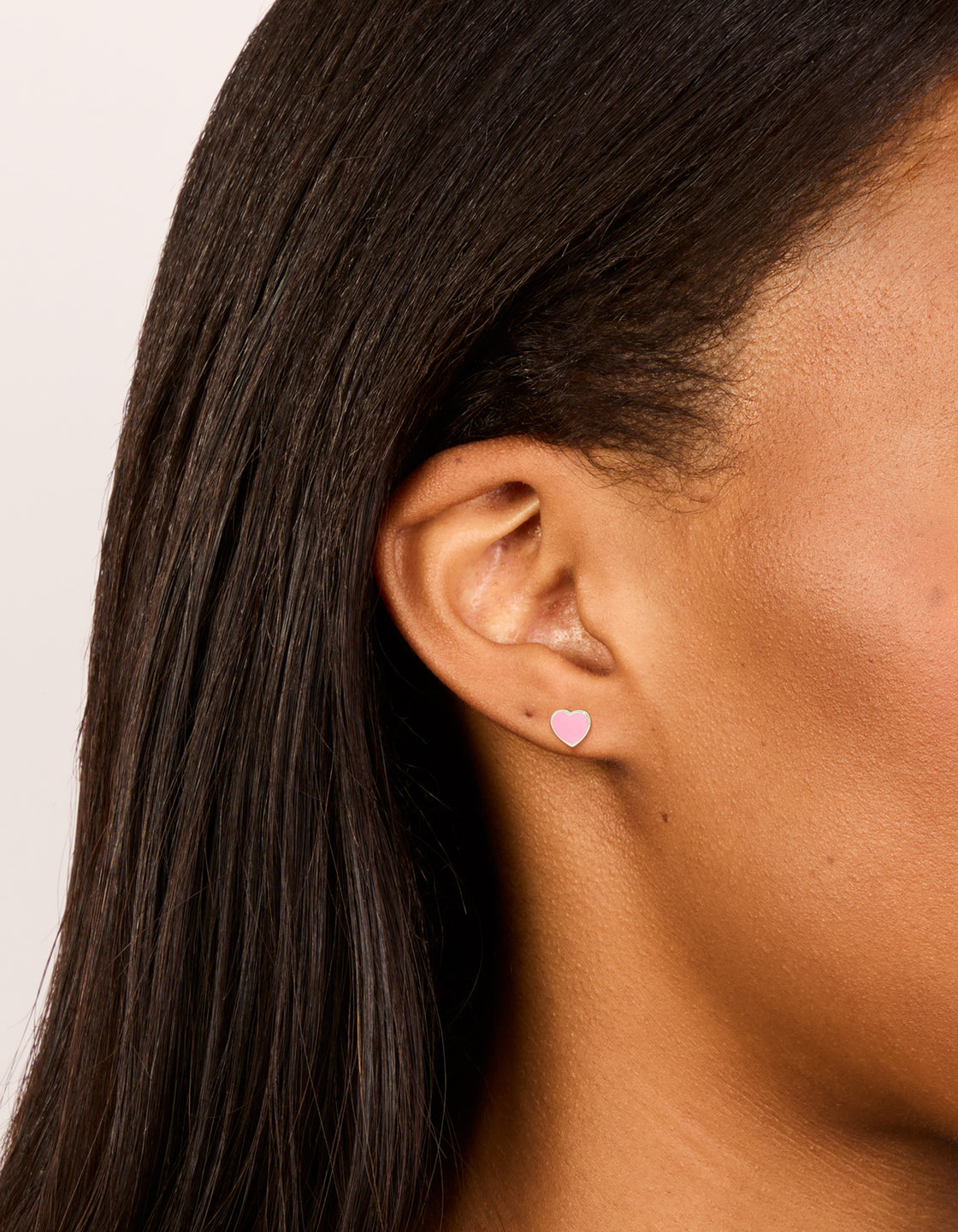 Showcasing dainty sterling silver pink enamel heart stud earrings featuring stud closure in silver on ear view