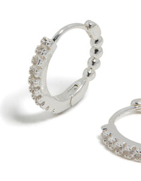 Featuring skinny huggie earrings in silver plated finish with cubic zirconia hoop closure close up view - link has visual effect only