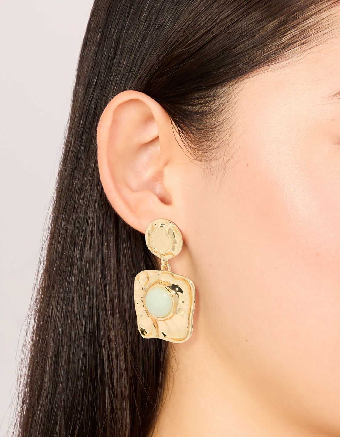 Showcasing statement drop earrings in gold with pale green stone featuring molten square design on ear view