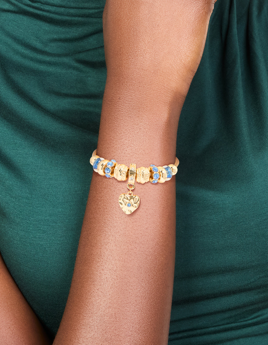 Showcasing a gold blue diamante and molten heart charm toggle bracelet with beaded and balls details on wrist view