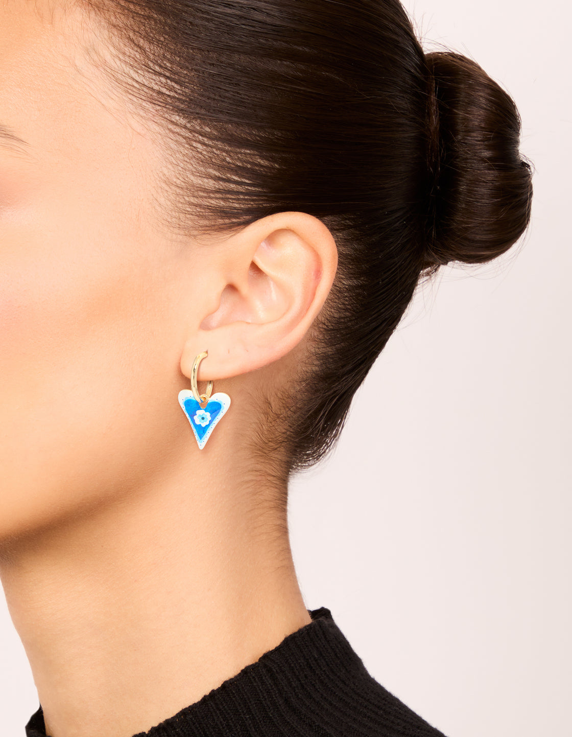 Showcasing gold blue heart huggie earrings with a flower inside featuring floral pattern on ear view