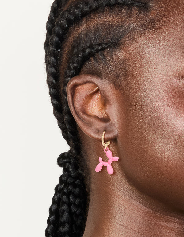 Showcasing huggie earrings in gold with pink balloon dog animal worn on ear view