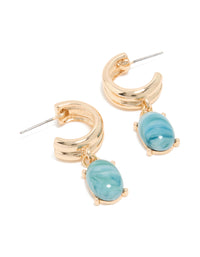 Showcasing statement huggie hoop earrings in gold with blue acrylic drop charms front view - link has visual effect only