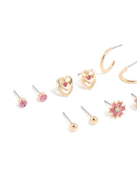 Featuring stud earrings 7-pack with balls, floral, butterfly, and heart motifs in gold with hot pink diamante stones close up view - link has visual effect only