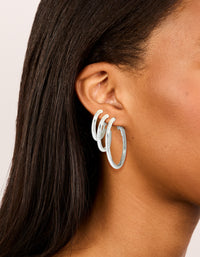 Showcasing silver plated thick hoop earrings in a statement and chunky 3-pack on ear view - link has visual effect only