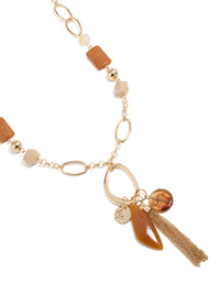 Showcasing a long beaded necklace featuring balls, beads, charm details, and tassel fringe in gold with statement styling close up view - link has visual effect only