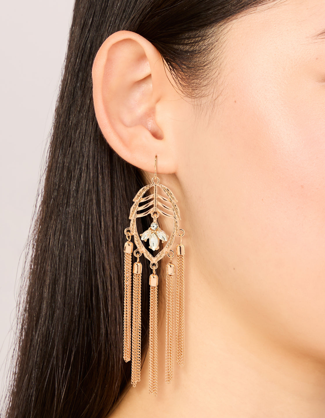 Elegant statement charm tassel drop earrings in gold with leaf and clear diamante details on ear view