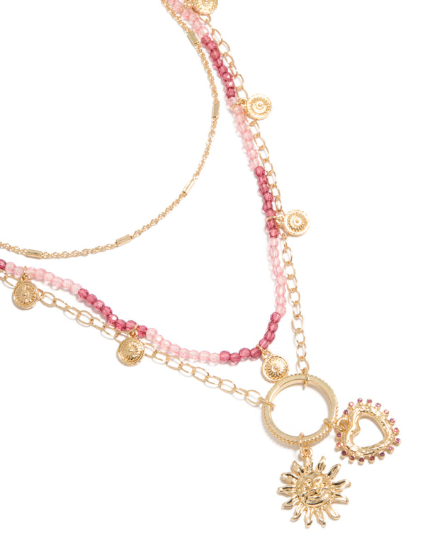 Showcasing a gold pink beaded and celestial layered necklace with charm featuring sun and heart in a statement design close up view