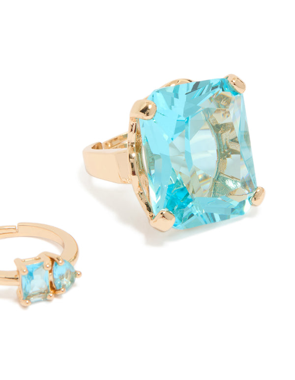 Featuring clear and blue oversized diamante rings in gold with oval stone cut, chunky statement style close up view