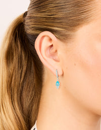Beautifully crafted silver plated cubic zirconia blue huggie drop earrings with crystal hoop closure in aqua on ear view - link has visual effect only