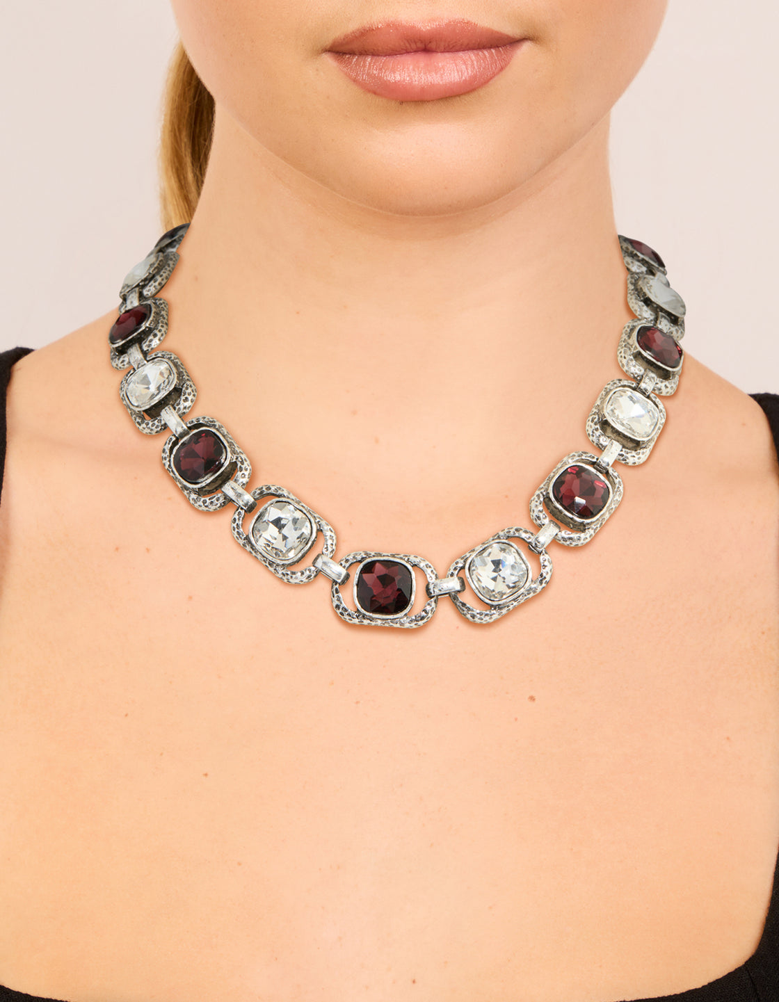 Showcasing a silver chunky necklace featuring clear and burgundy diamante accents on neck view
