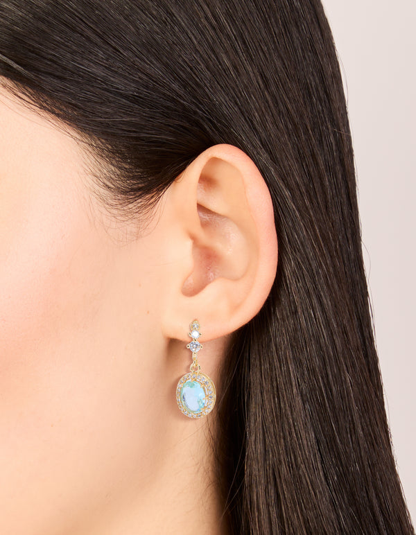 Featuring gold plated blue cubic zirconia oval halo drop earrings worn on ear to display scale and placement on ear view
